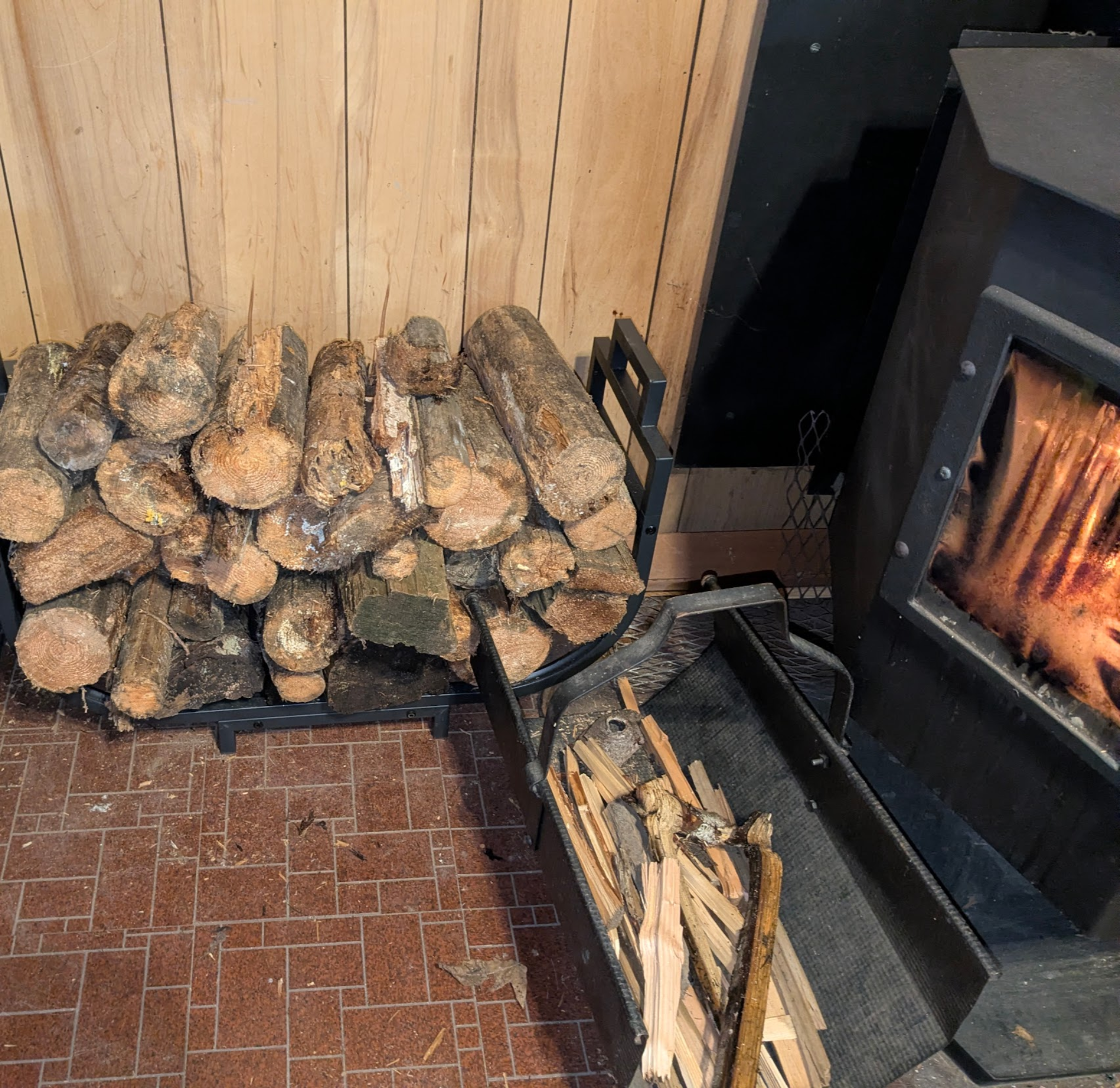 Wood stove with a fire burning, stacked firewood beside it
